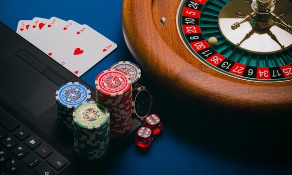 A laptop, playing cards, chips, dice, and a roulette wheel on a table